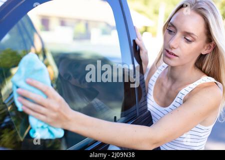 jeune femme essuyant sa voiture avec un chiffon en microfibre Banque D'Images