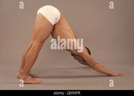 Yogi homme ne chien descendant Adho Mukha Svanasana yoga debout poser fond gris, asana Banque D'Images