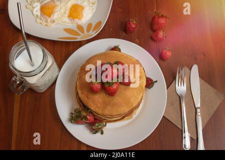 Assiette de gâteaux chauds avec fraises et œufs sur une table Banque D'Images