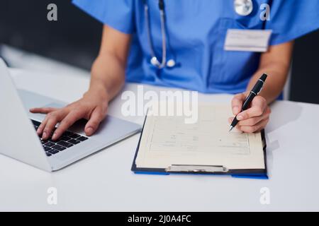 Garder ses dossiers à jour. Prise de vue en grand angle d'une infirmière féminine méconnue remplissant les documents administratifs tout en étant assise à son bureau à l'hôpital. Banque D'Images