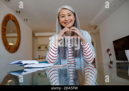 Femme gaie faisant un geste de coeur à la maison Banque D'Images