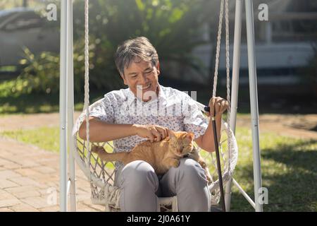Homme senior tenant un chat de gingembre en fauteuil roulant dans l'arrière-cour. Banque D'Images
