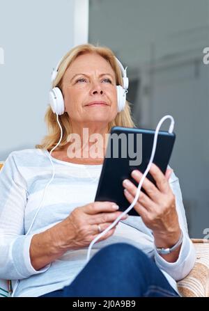 Vivre la vie d'un adolescent. Prise de vue d'une femme âgée portant un casque tout en tenant sa tablette numérique. Banque D'Images