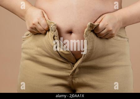 Femme en flabby grand ventre l'empêchant de mettre des jeans sur fond beige. Graisse viscérale. Corps positif. Gain de poids soudain. Serré peu Banque D'Images