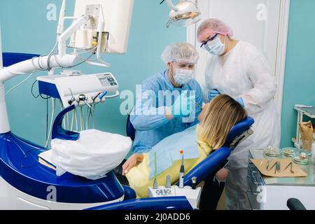 Une patiente en lunettes dentaires traite les dents du dentiste à la lumière ultraviolette. Plombages dentaires. Banque D'Images