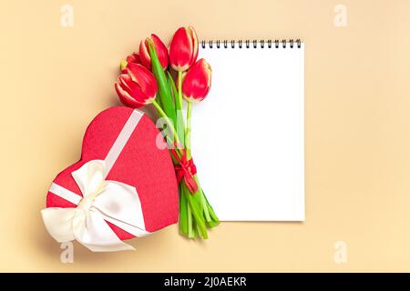 Bouquet de tulipes rouges, bloc-notes blanc sur fond beige vue du dessus plat Lay carte de vœux Happy Moter's day, 8 March, Valentine's Day, Easter concept Copy space maquette. Banque D'Images