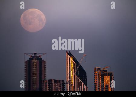 Londres, Royaume-Uni. 18th mars 2022. Météo au Royaume-Uni : le lever du soleil se lève le matin au-dessus de la ville et voit une pleine lune de 99,8 % vers les bâtiments, y compris la tour Strata SE1, dans le sud-est de Londres. Credit: Guy Corbishley/Alamy Live News Banque D'Images