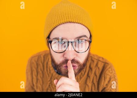 Gros plan d'un jeune homme caucasien barbu regardant la caméra montrant le geste hush shh isolé de fond orange focus sur la tête . Photo de haute qualité Banque D'Images