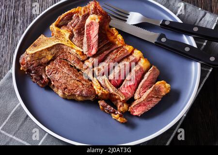 rôti de steak de portreuse en tranches, steak d'os de bœuf sur une assiette avec des couverts de steak sur une table en bois de chêne foncé, vue horizontale d'en haut, gros plan Banque D'Images