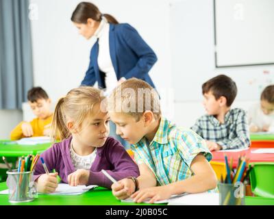 Les élèves heureux assis bavardant à leçon à l'école élémentaire Banque D'Images