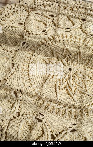 Tapis maison tricoté en fils épais, fait à la main: Un tapis fait à la main en fils beige se trouve sur le sol, le soleil brille dessus Banque D'Images