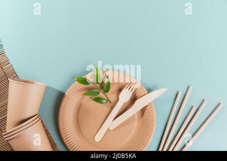 Vaisselle en papier jetable. Tasses, assiettes, fourchettes en bois, couteaux, cuillères et pailles sur fond bleu clair. Concept sans plastique et sans déchets. Banque D'Images