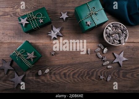 Cadre de Noël avec boîtes cadeaux, décorations en étoile en bois et cônes en sapin sur fond de bois sombre. Arrière-plan de vacances dans des couleurs naturelles de terre. Banque D'Images