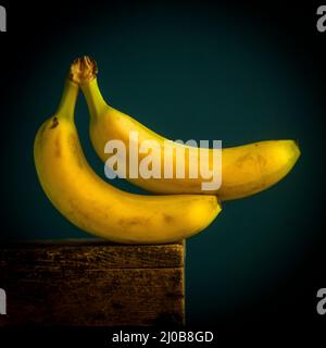 Deux bananes mûres reposant sur une table en bois sur un fond bleu foncé Banque D'Images