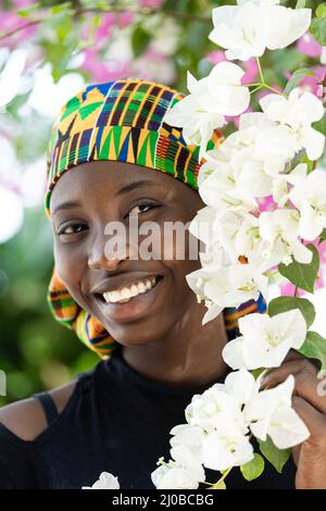 Portrait d'une magnifique fille ouest-africaine souriante qui se pose parmi des fleurs de bougainvilliers blanc et rose - un symbole de la jeunesse, de la beauté et du bonheur Banque D'Images