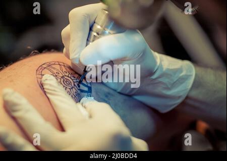 Le tatouage maître dessine la peinture bleue sur le tatouage client Banque D'Images