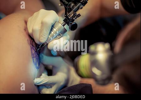 Le tatouage maître dessine la peinture bleue sur le tatouage client Banque D'Images