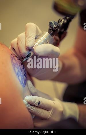 Le tatouage maître dessine la peinture bleue sur le tatouage client Banque D'Images