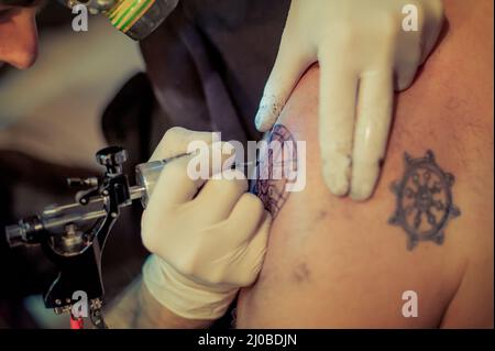 Le tatouage maître dessine la peinture bleue sur le tatouage client Banque D'Images