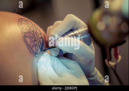 Le tatouage maître dessine la peinture bleue sur le tatouage client Banque D'Images