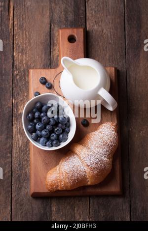 Croissant au lait et aux mûres sur une planche de bois. Vue de dessus Banque D'Images