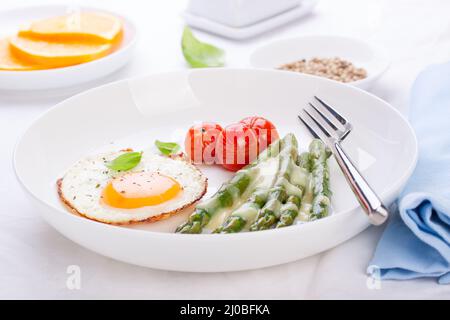 Œuf frit avec asperges et tomates sur une assiette blanche avec serviette bleue. Banque D'Images