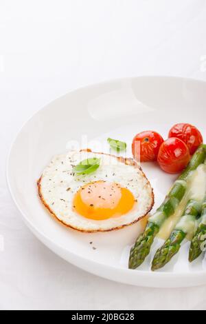 Œuf frit avec asperges et tomates sur une assiette blanche avec serviette bleue. Banque D'Images