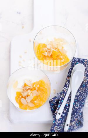 Compote de pêches et de poires sucrées avec yaourt dans un verre et confiture sur un tableau blanc Banque D'Images