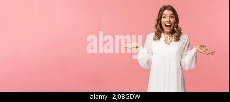 Surprise et heureuse jeune fille blonde réaliser qu'elle a gagné, recevoir vraiment de bonnes nouvelles, se répandre les mains sur le côté souriant et regarder étonné de l'appareil photo, debout rose Banque D'Images