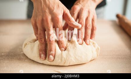 Les mains de la femme pétrir de la pâte sur la table dans sa cuisine. Gros plan Banque D'Images