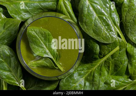 Vue de dessus d'un bol en verre rempli d'un smoothie aux légumes d'épinards entouré de feuilles d'épinards crues. Banque D'Images