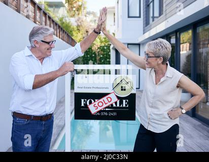 Un autre client heureux. Coupe courte de deux personnes mûres de haut cinq en se tenant devant un tableau à vendre avec un autocollant vendu dessus. Banque D'Images
