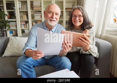 Heureux couple aînés utilisant tablette informatique en ligne faisant la planification financière ensemble à la maison Banque D'Images