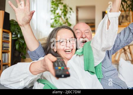 Encourager un couple senior à utiliser la télécommande tout en regardant la télévision dans le salon à la maison Banque D'Images