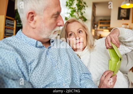 Un couple âgé inquiet avec un portefeuille vide à la maison sur un canapé comme symbole de pauvreté dans la vieillesse Banque D'Images