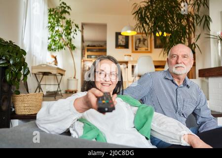 Couple senior regardant avec la télécommande de la télévision tout en regardant dans le salon à la maison Banque D'Images