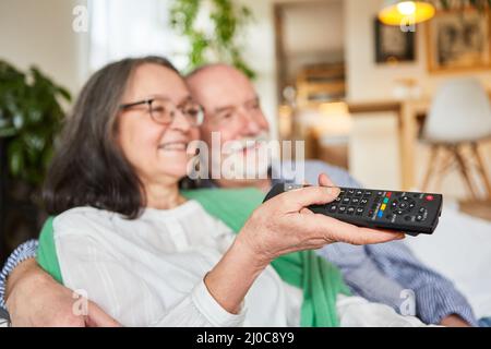 Couple senior avec télécommande assis détendu regardant la télévision dans le salon à la maison Banque D'Images