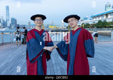 Deux heureux et fiers doctorants diplômés de sexe masculin dans la robe académique secouer les mains et se féliciter l'un l'autre Banque D'Images