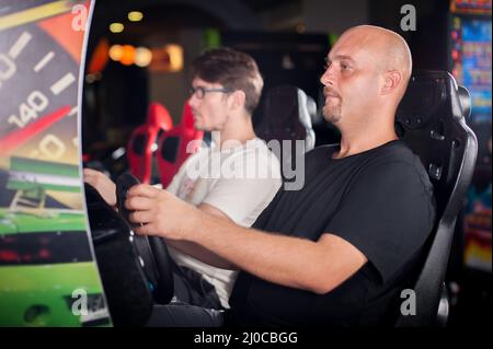 Jeune homme jouant à la roue de conduite jeu vidéo dans la salle de jeux Banque D'Images