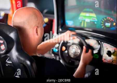 Jeune homme jouant à la roue de conduite jeu vidéo dans la salle de jeux Banque D'Images