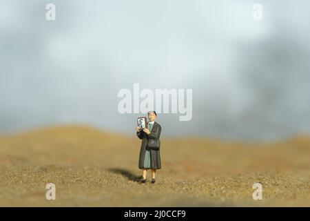 Photographie miniature de personnage de jouet de personnes. Une femme tenant un cadre photo, recherchant la personne manquante en raison d'un conflit de guerre dans le désert. Photo d'image Banque D'Images