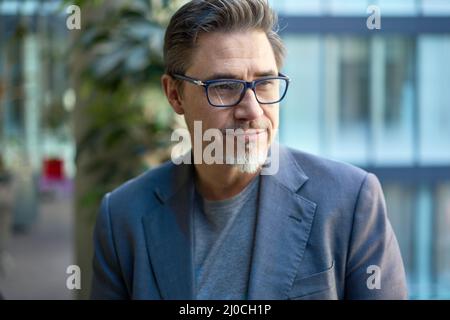 Homme d'affaires d'un âge moyen et confiant dans un cadre professionnel décontracté au bureau. Portrait d'un homme mi-adulte heureux en 50s, souriant, regardant loin. Banque D'Images