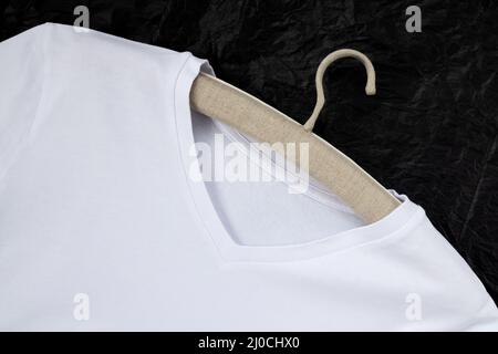 Maquette d'un t-shirt en coton blanc, sur un cintre en lin. Gros plan, arrière-plan noir Banque D'Images