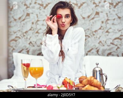 Profitez d'un petit déjeuner qui vous donnera un petit coup de pouce. Prise de vue d'une jeune femme attrayante prenant un petit déjeuner luxueux dans sa chambre. Banque D'Images