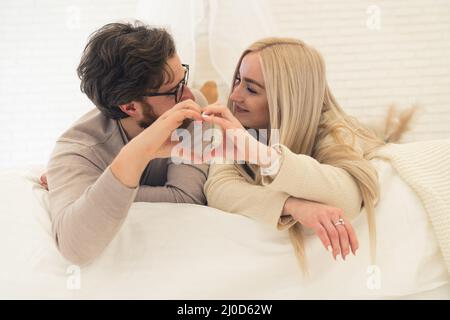 adorable jeune couple allongé sur le lit faisant une forme de coeur avec leurs mains. Photo de haute qualité Banque D'Images