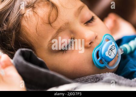 Un bébé dormant avec une sucette bleue Banque D'Images