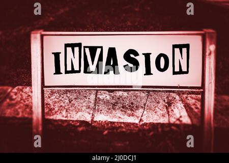 Le mot invasion est affiché sur un panneau de rue avec du texte noir sur fond blanc dans un rouge sombre et noir monotone avec une police de style note de rançon Banque D'Images