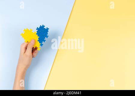 Contexte de la journée du syndrome de Down du monde. Enfants mains tenant bleu et jaune vers le bas conscience coeur de jour sur fond jaune pastel et bleu. Haut Banque D'Images