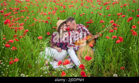 couple amoureux de l'homme et de la femme avec guitare acoustique dans le champ de fleurs de pavot d'été, date romantique Banque D'Images