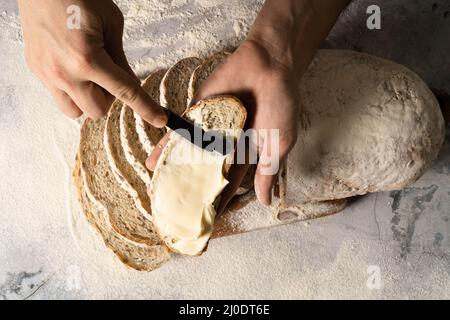 Homme en train de répartir le beurre de fromage à la crème ou une tranche de pain sur une planche à bois. Le pain à la diète. Gros plan. Concept de nutrition saine. Banque D'Images